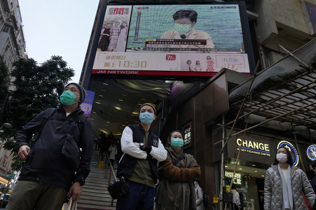 People wearing protective face masks walk around Hong Kong’s shopping areas while a TV screen broadcasts measures to counter the coronavirus outbreak. Photo: AP