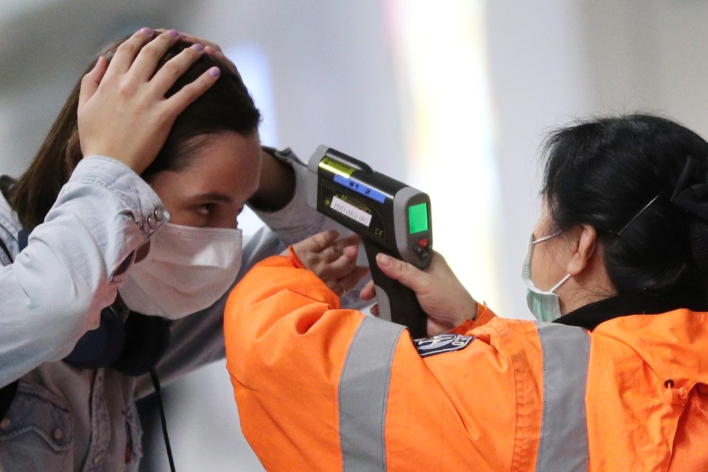 A worker uses an infrared thermometer to check the temperature of a passenger arriving at Hong Kong International Airport. Photo: Reuters