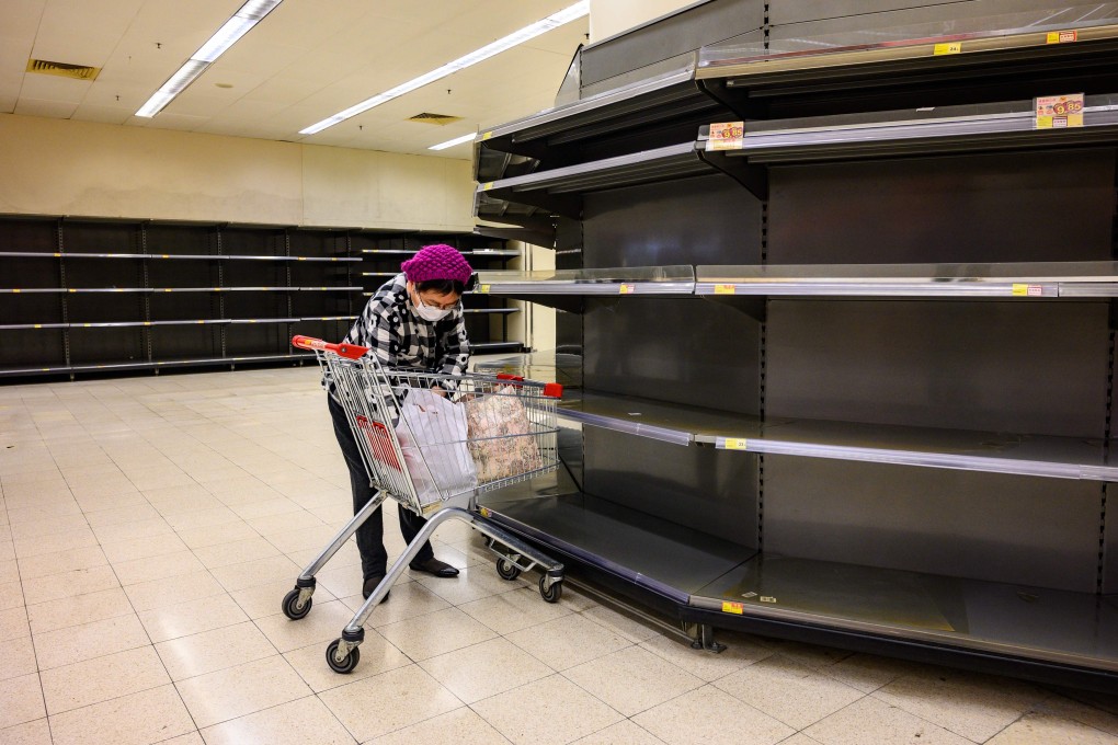 A shopper wearing a face mask sorts items in her trolley as she stands next to bare supermarket shelves, usually stocked with toilet paper and kitchen rolls, in Hong Kong on February 6. Panic buyers in Hong Kong have descended on supermarkets to snap up toilet paper after false online claims of shortages, prompting authorities to appeal for calm. Photo: AFP