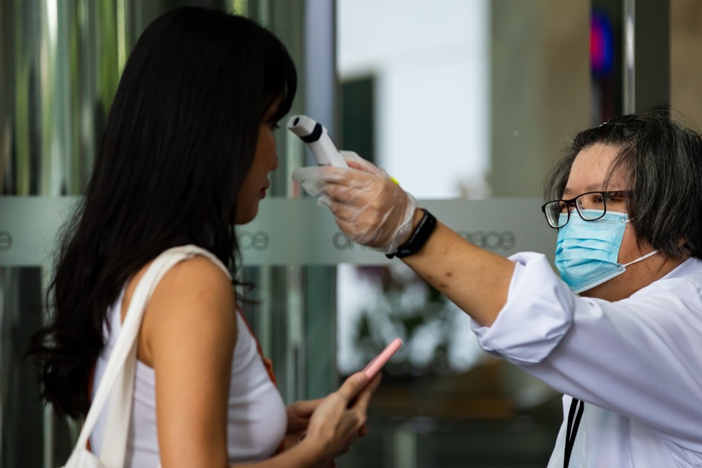 A security guard wearing a protective mask checks the temperature of a person entering an office building in Singapore. Photo: Bloomberg