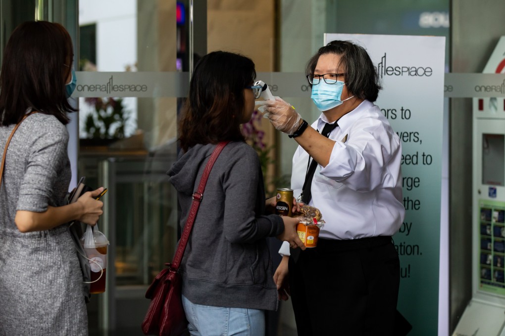 A security guard wearing a protective mask checks the temperature of a person entering an office building in the central business district of Singapore. The city state on Thursday reported eight new coronavirus cases. Photo: Bloomberg