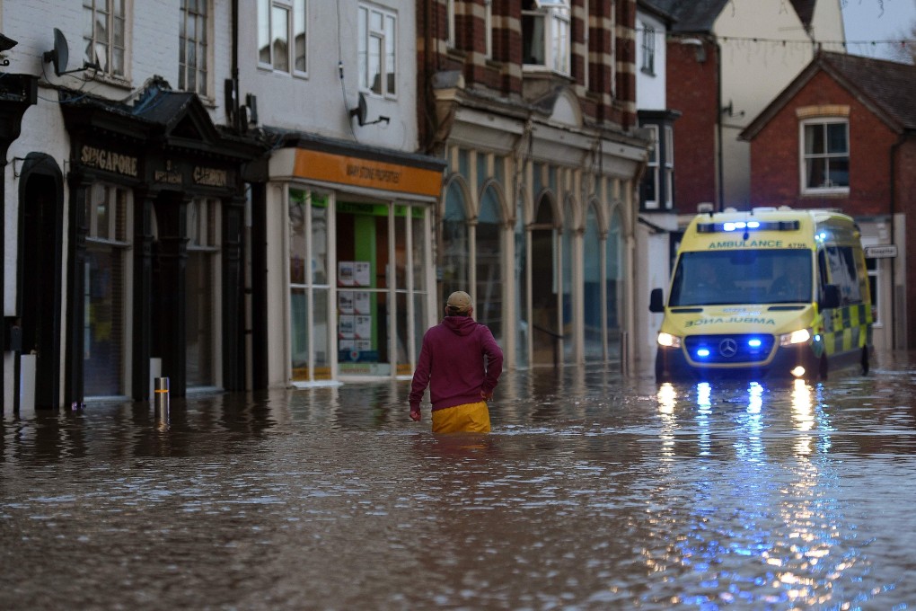 A man wades through floodwater towards an ambulance in a flooded street in Tenbury Wells. Photo: AFP