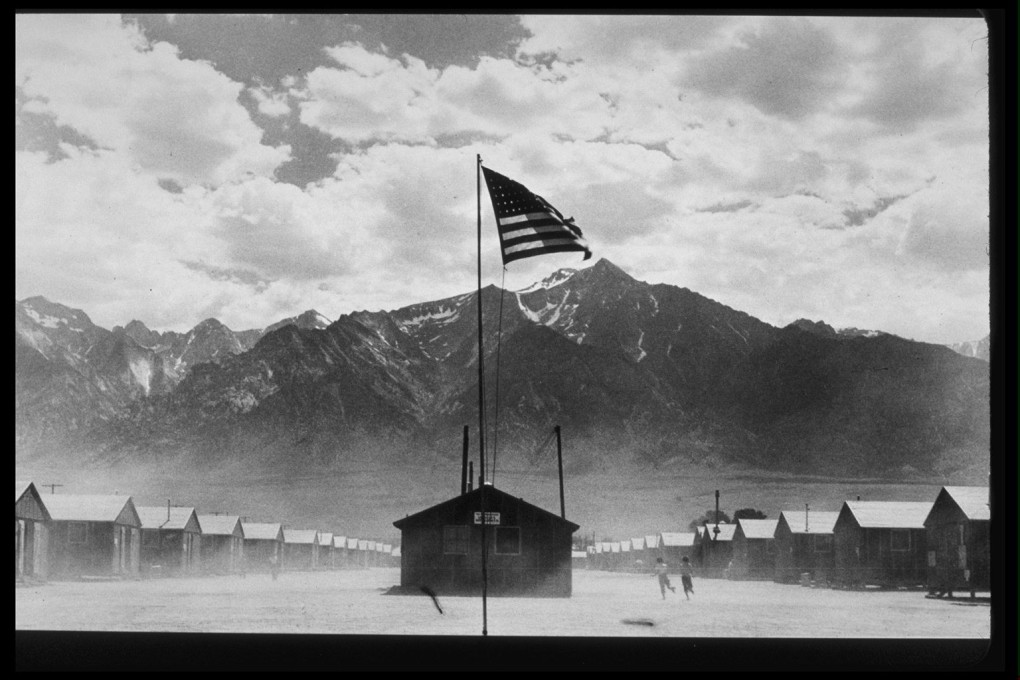 Mountains overlook a Japanese-American relocation camp in Manzanar, California, July 1942. A US flag waves in the foreground.