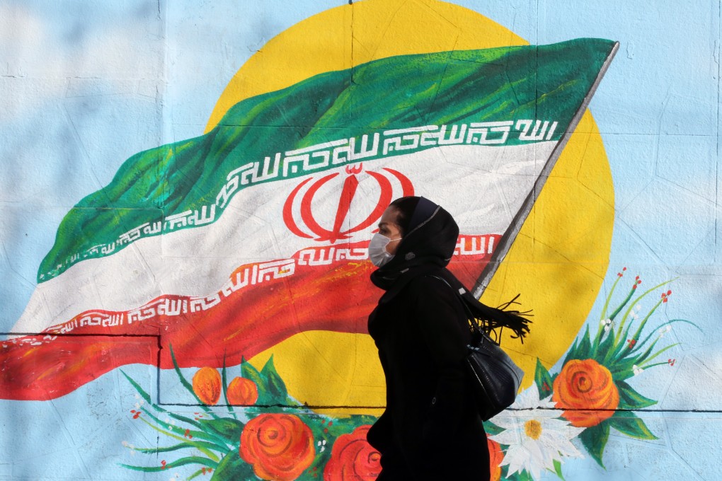 An Iranian woman wearing a mask walks next to a wall painting of the Iranian national flag in Tehran. Photo: EPA-EFE