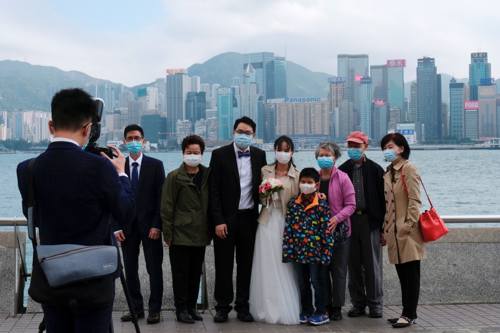 A newlywed couple and their family, all wearing protective masks, take a photo in Tsim Sha Tsui on February 24. Life must go on and Hongkongers must get back to work. Photo: Reuters