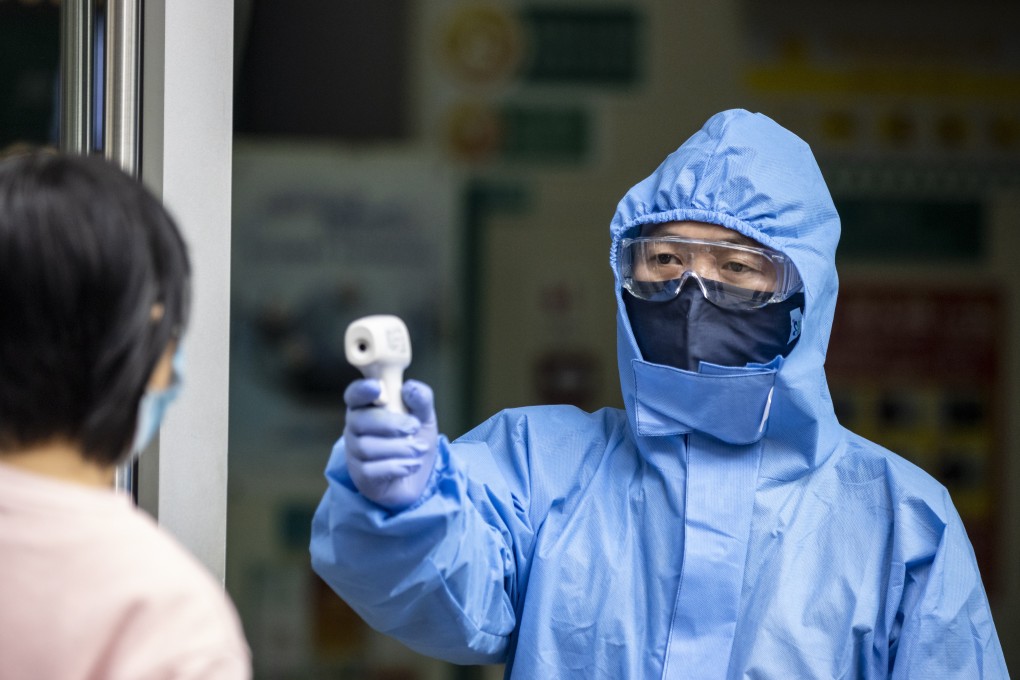 A security guard in protective gear measures visitors’ body temperatures at the entrance to a bank in Guangzhou, China, on February 24, 2020. Photo: EPA