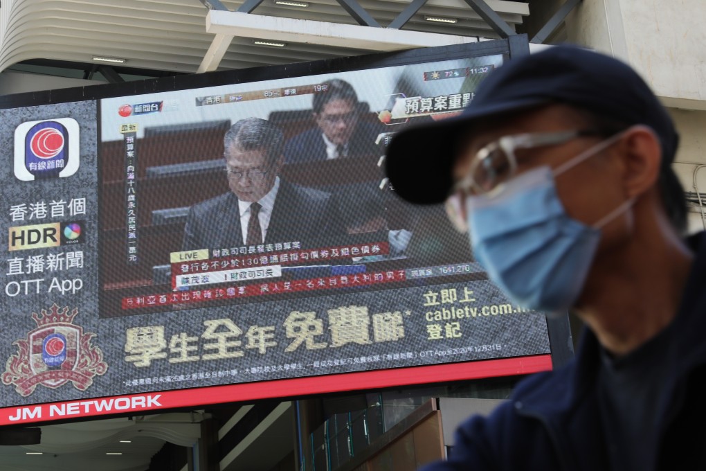 A man wearing a mask walks past a television screen streaming Financial Secretary Paul Chan delivering the budget, in Causeway Bay. Photo: Dickson Lee