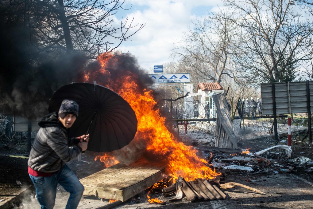 A man takes cover behind an umbrella as he throws a mattress in a fire during clashes with Greek police in the buffer zone at Turkey-Greece border, at Pazarkule. Photo: AFP