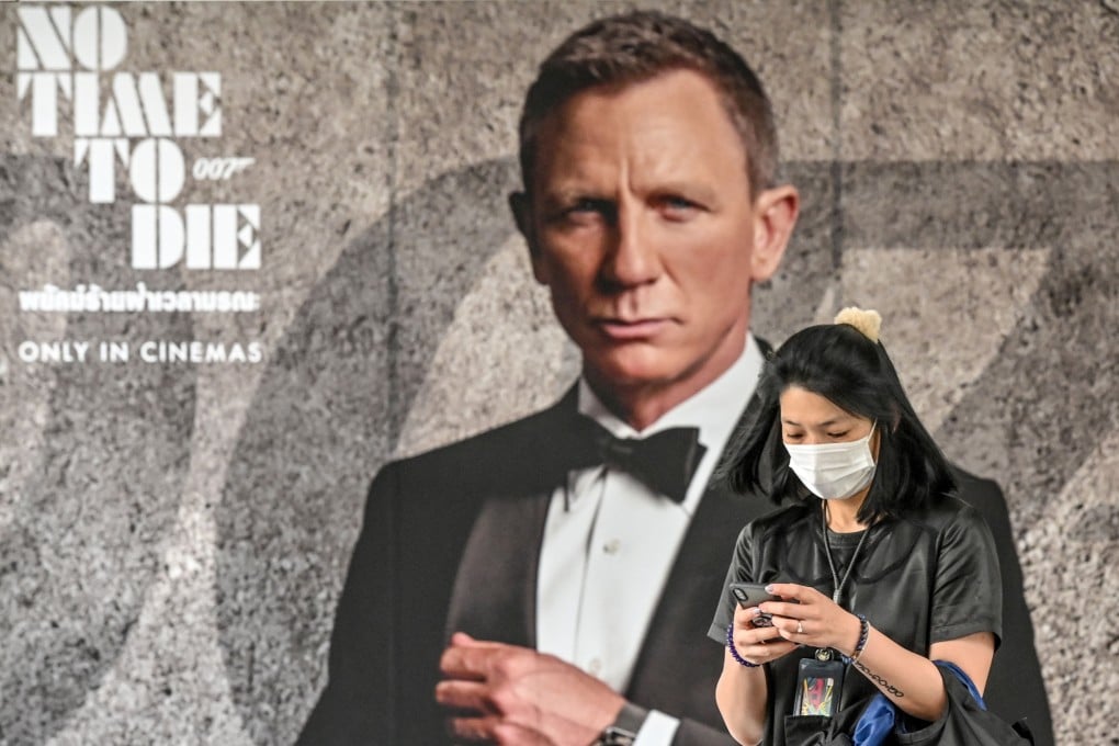 A woman wearing a face mask walks past a poster for the new James Bond movie “No Time to Die” in Bangkok in February. Photo: AFP