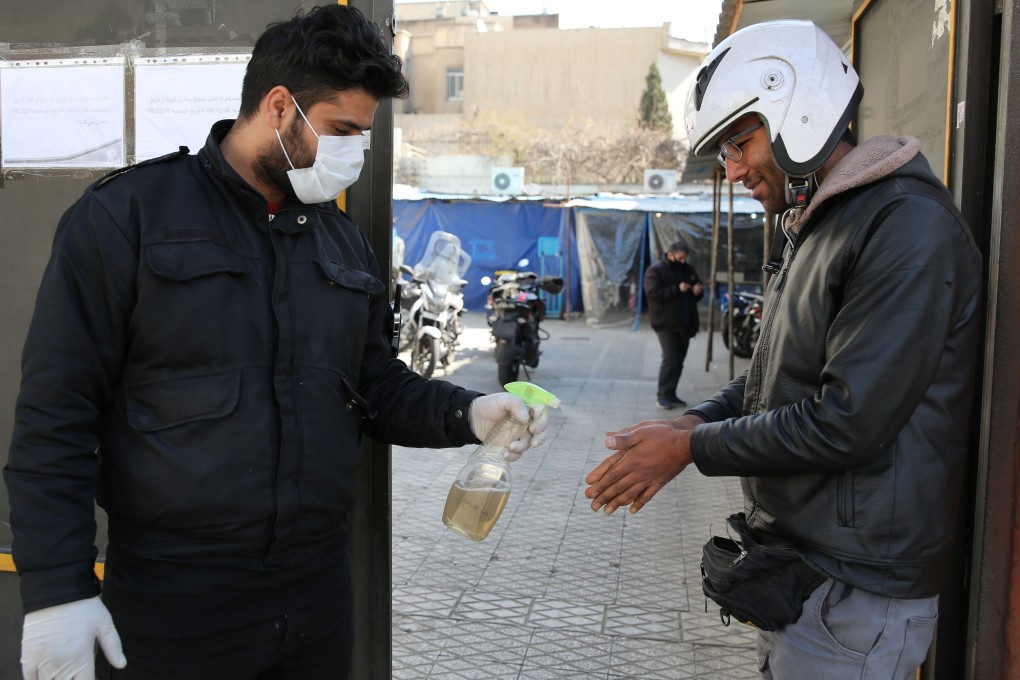 A man sprays alcohol on the hands of clients outside an office building in Tehran. Photo: AFP