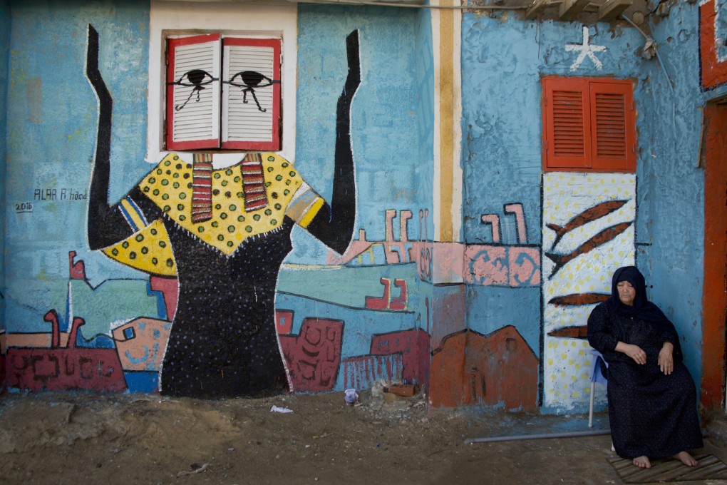 An Egyptian woman sits in front of a mural by artist Alaa Aboul Hamad in Burullus, north of Cairo, in October 2016. Photo: AP