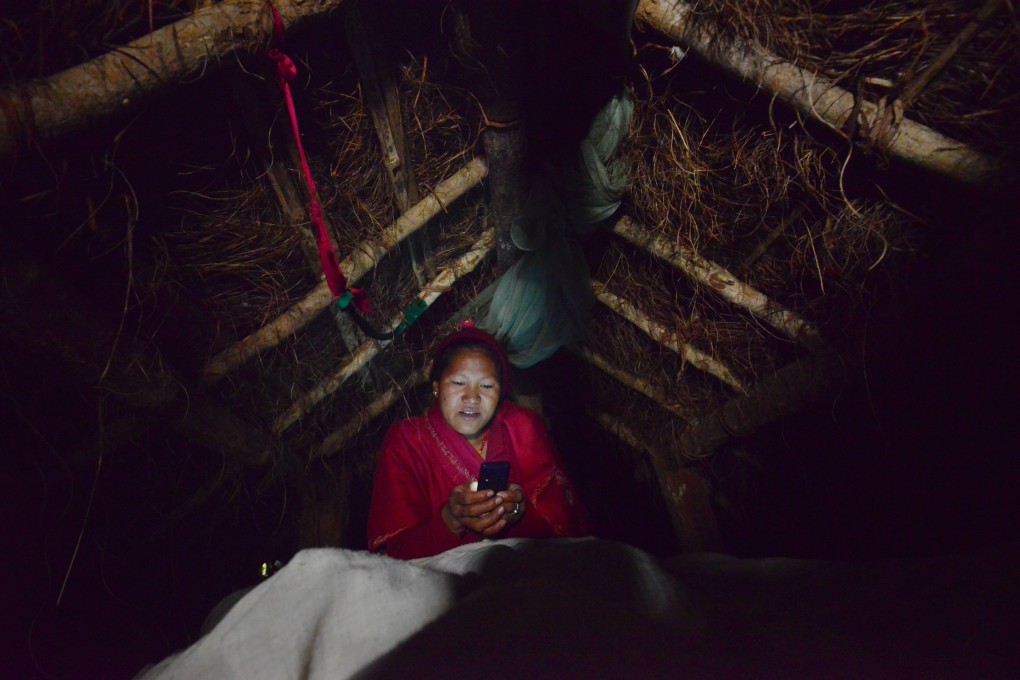 A Nepalese woman looks at her mobile phone in a hut to which she has been banished during her menstruation. Women undergoing their period are forced into a monthly exile in basic huts, and barred from touching food, religious icons, cattle and men. Photo: Prakash Mathema/AFP