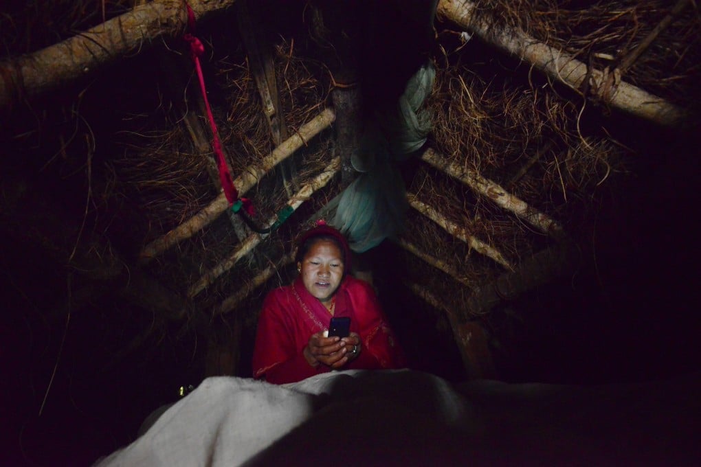 A Nepalese woman looks at her mobile phone in a hut to which she has been banished during her menstruation. Women undergoing their period are forced into a monthly exile in basic huts, and barred from touching food, religious icons, cattle and men. Photo: Prakash Mathema/AFP