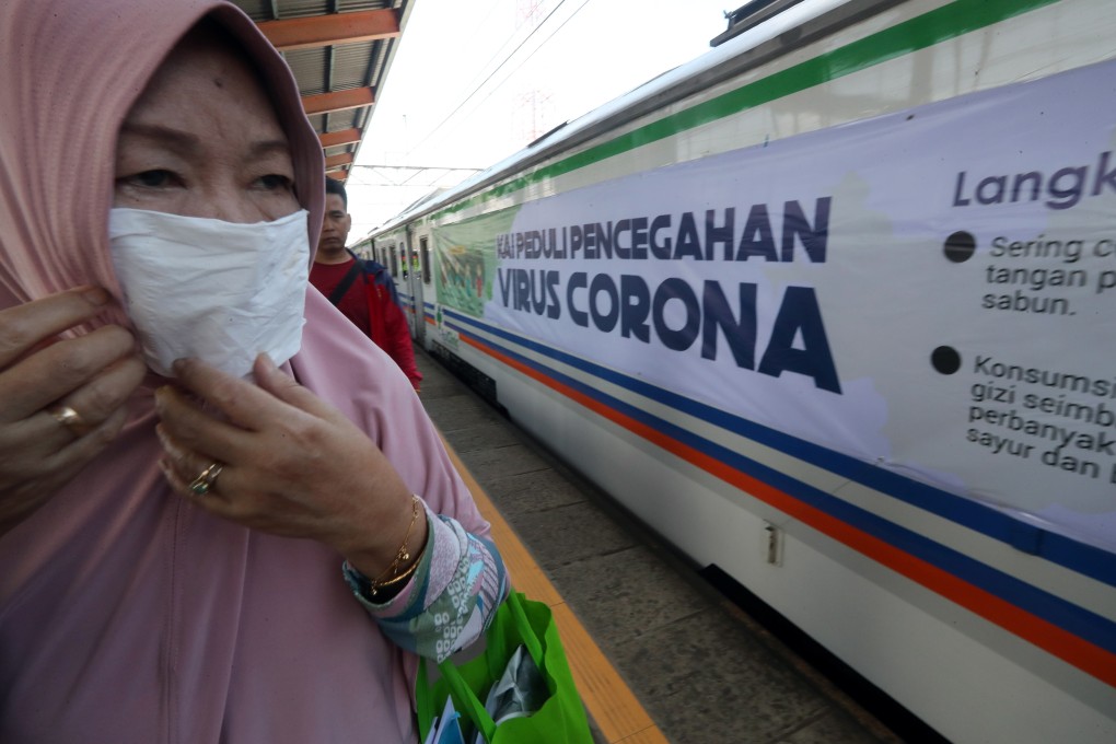 An Indonesian train passenger wears a mask as she walk past a banner reading ‘Coronavirus Prevention’ in West Java. Photo: EPA