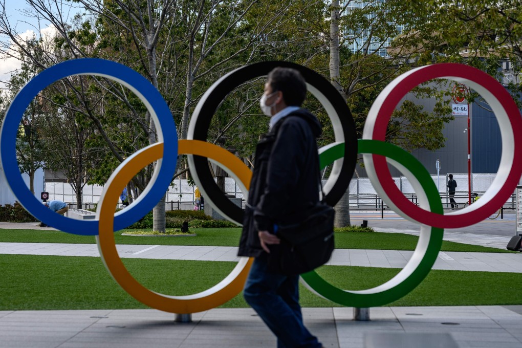 A man wearing a face mask walks in front of the Olympic Rings in Tokyo. There are increasing calls to delay the Summer Games. Photo: AFP