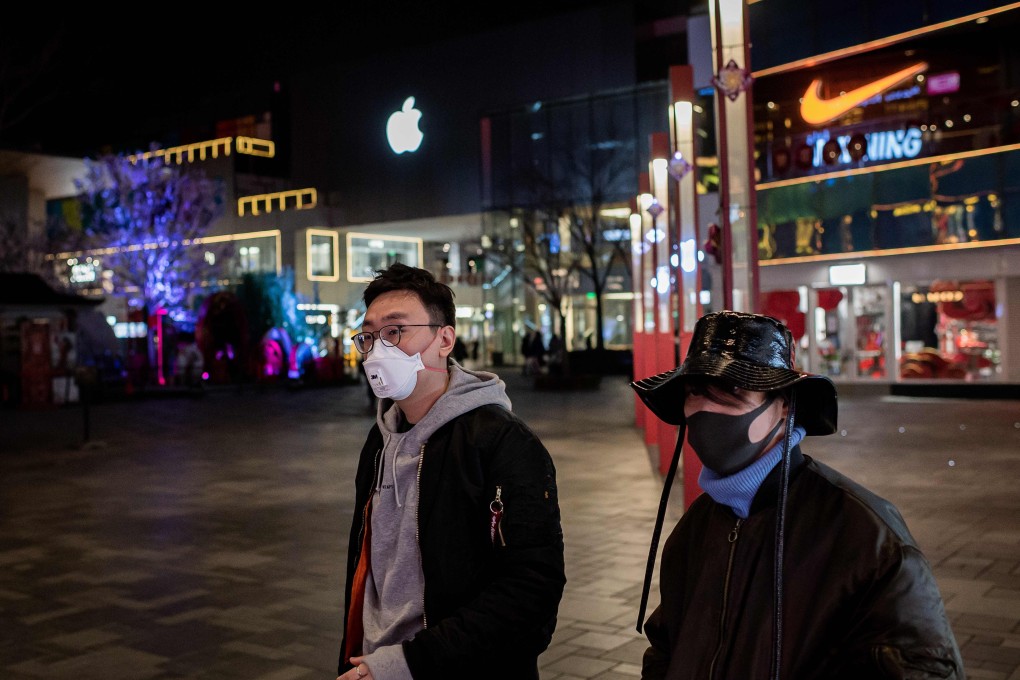 People wearing a protective facemask to protect against the COVID-19 coronavirus walk past an Apple store outside of a nearly empty shopping mall in Beijing on February 24, 2020. Photo: AFP