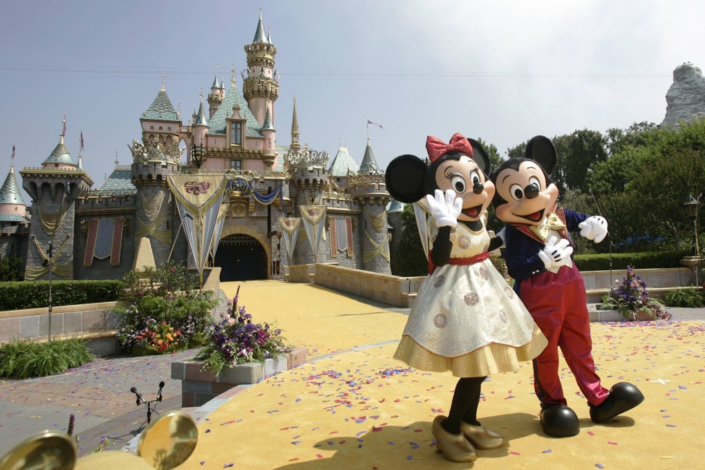 Employees in Mickey and Minnie Mouse costumes wave in front of the Sleeping Beauty Castle at Disneyland in Anaheim, California, in July 2005. Photo: AFP