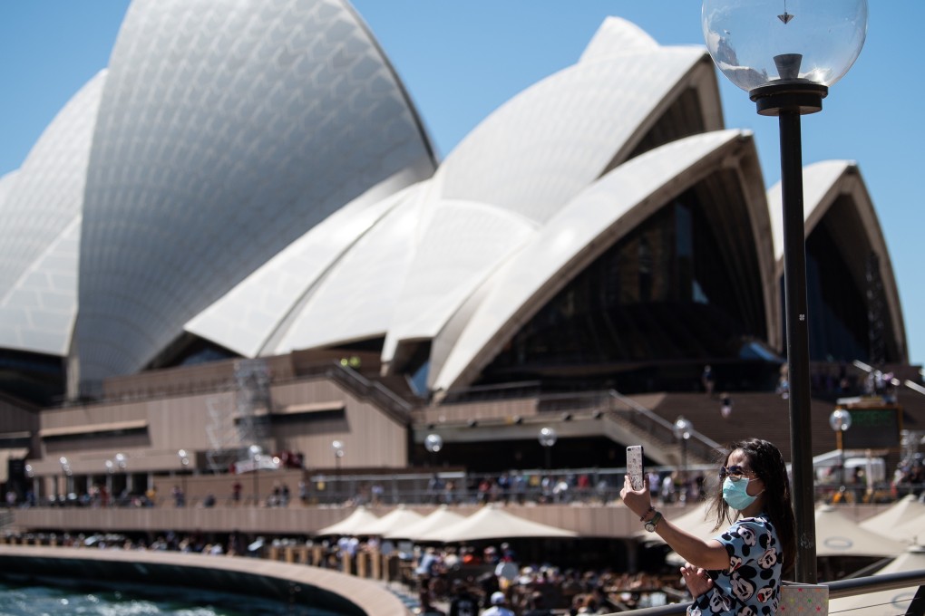 A woman wearing a face mask takes a photo near the Sydney Opera House in Sydney, Australia on Friday. Photo: EPA