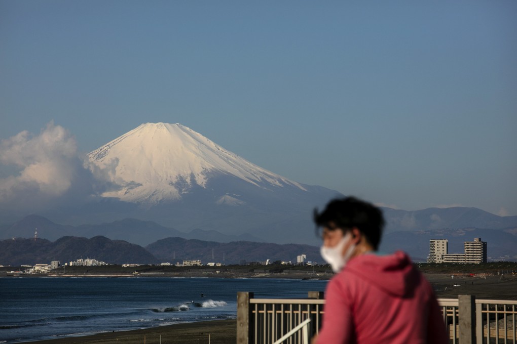 A snow-capped Mount Fuji is in the background as a mask-wearing man visits the beach. Photo: AP