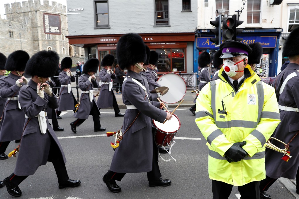 A security guard wearing a face mask stands outside Windsor Castle in the UK as a marching band passes by on Tuesday. Photo: Reuters
