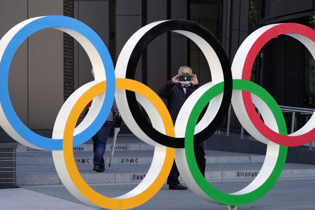 A man wearing a mask takes pictures of an Olympic Rings monument in front of the Japan Olympic Committee headquarters in Tokyo. Photo: EPA