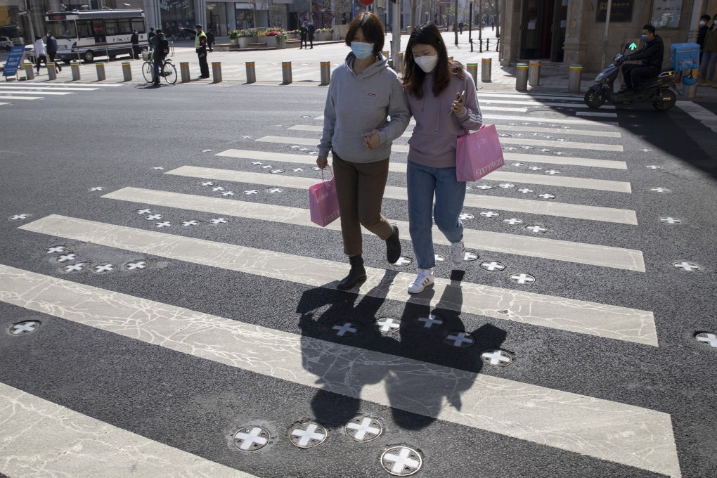 Masked shoppers cross the road near a deserted shopping district in Beijing on March 22. China is striving to restore activity in the world’s second-largest economy. Photo: AP