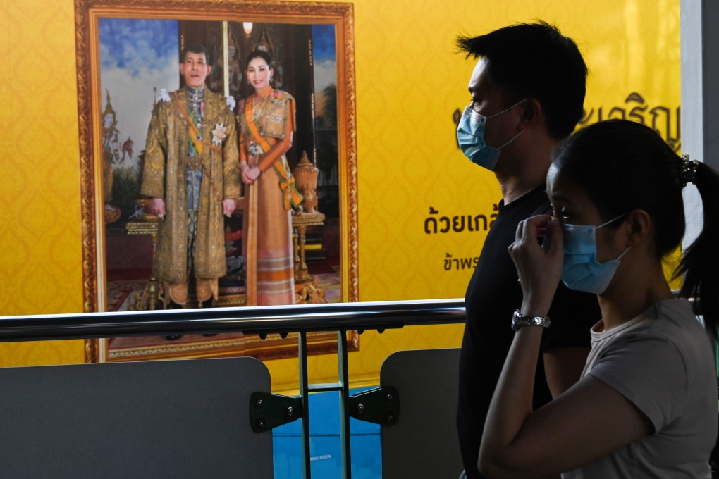 Thais wearing face masks pass a billboard bearing the portrait of King Maha Vajiralongkorn and Queen Suthida. Photo: AFP