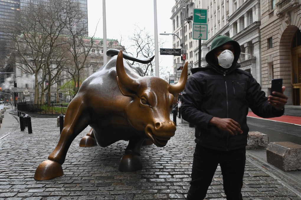 A man wearing a face mask takes a picture at the charging bull statue near the New Stock Exchange on Monday. Stocks on Wall Street fell early as Congress wrangled over a massive stimulus package. Photo: AFP