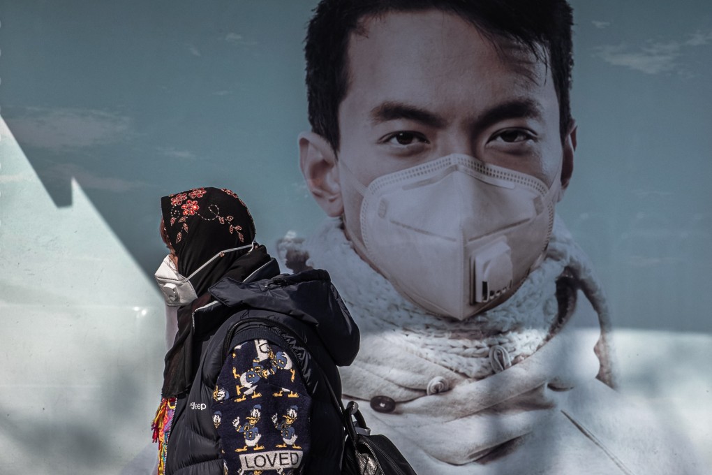 A person wearing a face mask walks past a face mask advertisement in Beijing. Photo: EPA-EFE