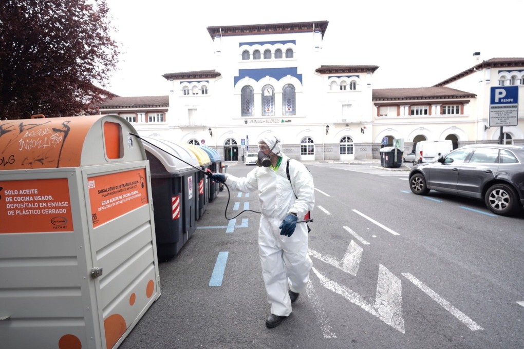 A municipal employee wearing protective gear disinfects trash bins in Vitoria, Basque Country, Spain on Tuesday. Photo: EPA-EFE