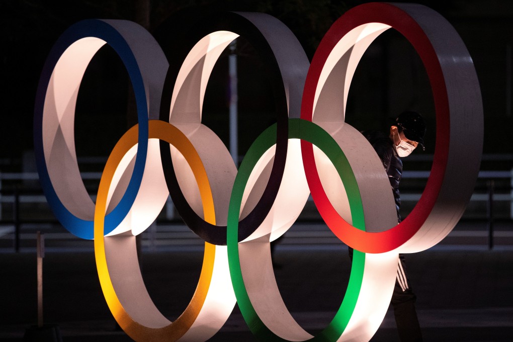 A man wearing a protective face mask looms at the Olympic rings in Tokyo. Photo: Reuters