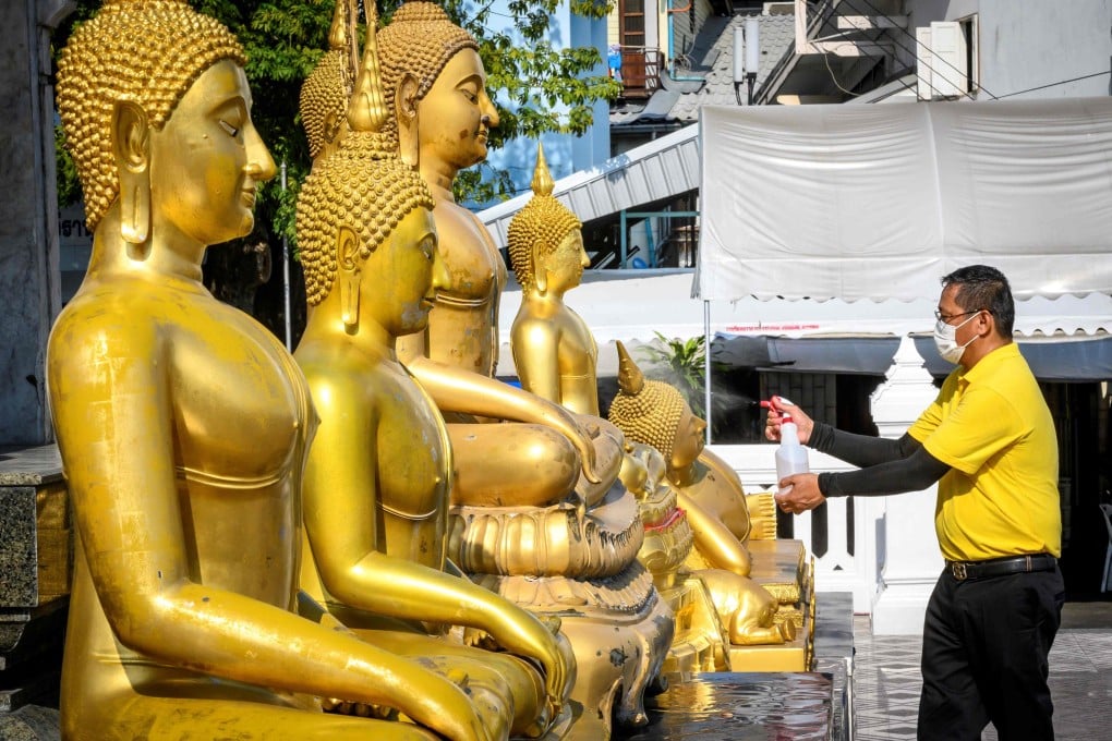 A volunteer disinfects Buddha statues before a televised anti-plague prayer at Wat Traimit Temple, Bangkok, amid lockdown restrictions to contain the spread of the coronavirus. Photo: AFP