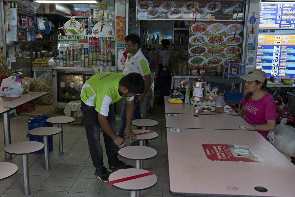A worker puts tape on stools as a social distancing marker at a food centre in Singapore. Photo: Bloomberg
