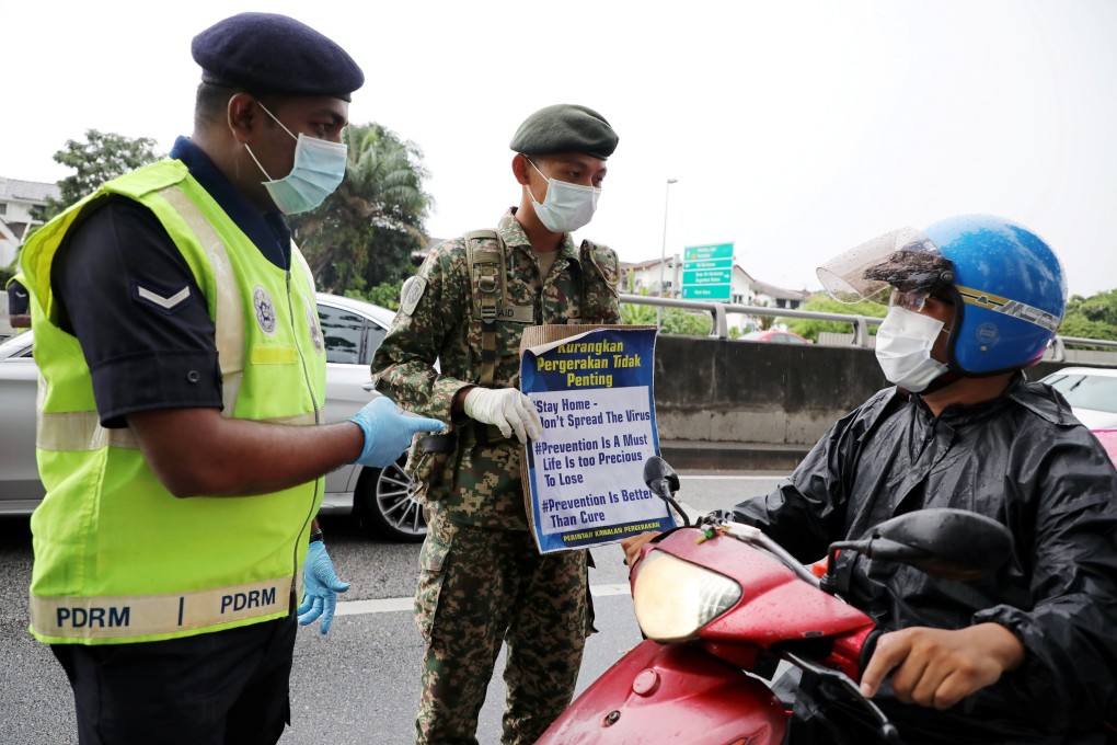 A soldier and a police officer wearing protective masks stop a motorcyclist at a roadblock set up to enforce a movement control order due to the outbreak of the coronavirus disease in Malaysia. Photo: Reuters