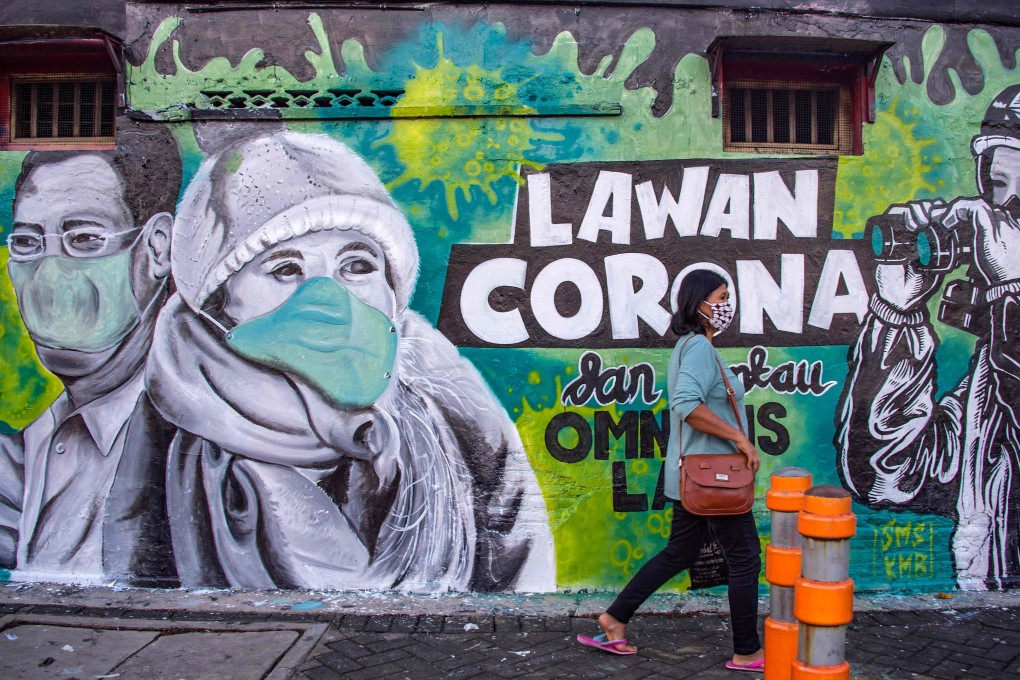 An Indonesian woman in Surabaya, East Java, walks past a mural asking people to join the fight against the coronavirus. Photo: AFP