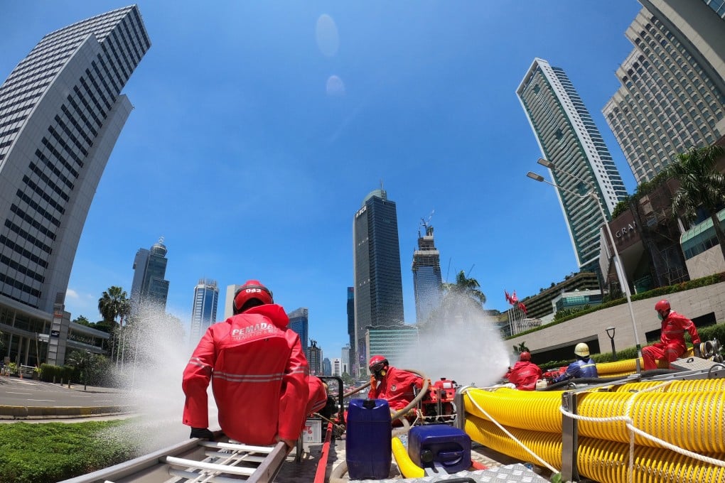 Firefighters sit on high pressure pump trucks as they spray disinfectant in Jakarta, Indonesia, on Tuesday. Photo: Reuters