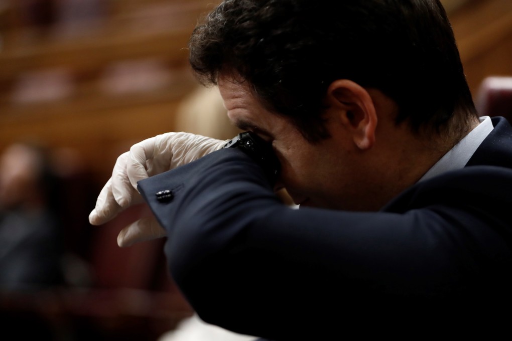 A Spanish member of parliament touches his eye with his wrist. Photo: EPA