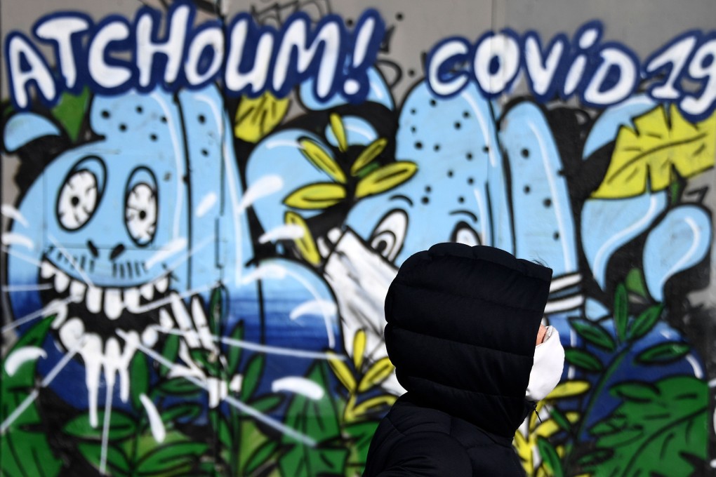 A jogger wearing a face mask passes a mural with the message “Achoo Covid-19” in Paris on Wednesday. Photo: AFP
