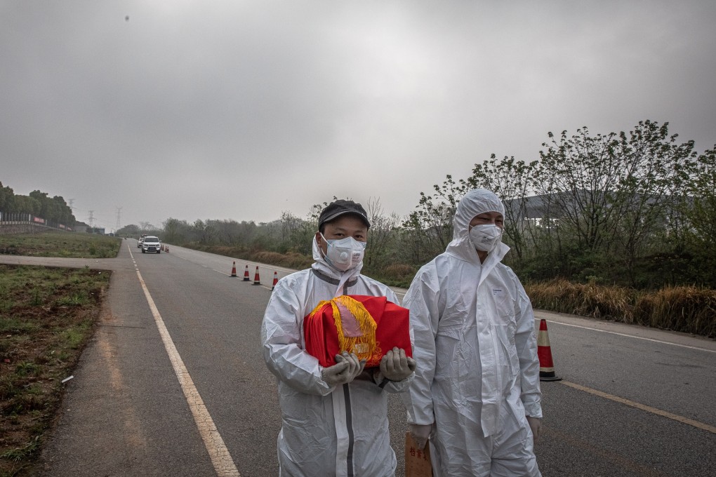 A man wearing a full protective outfit carries a box containing the ashes of a deceased relative next to a funeral house in Wuhan, on April 1. Photo: EPA-EFE