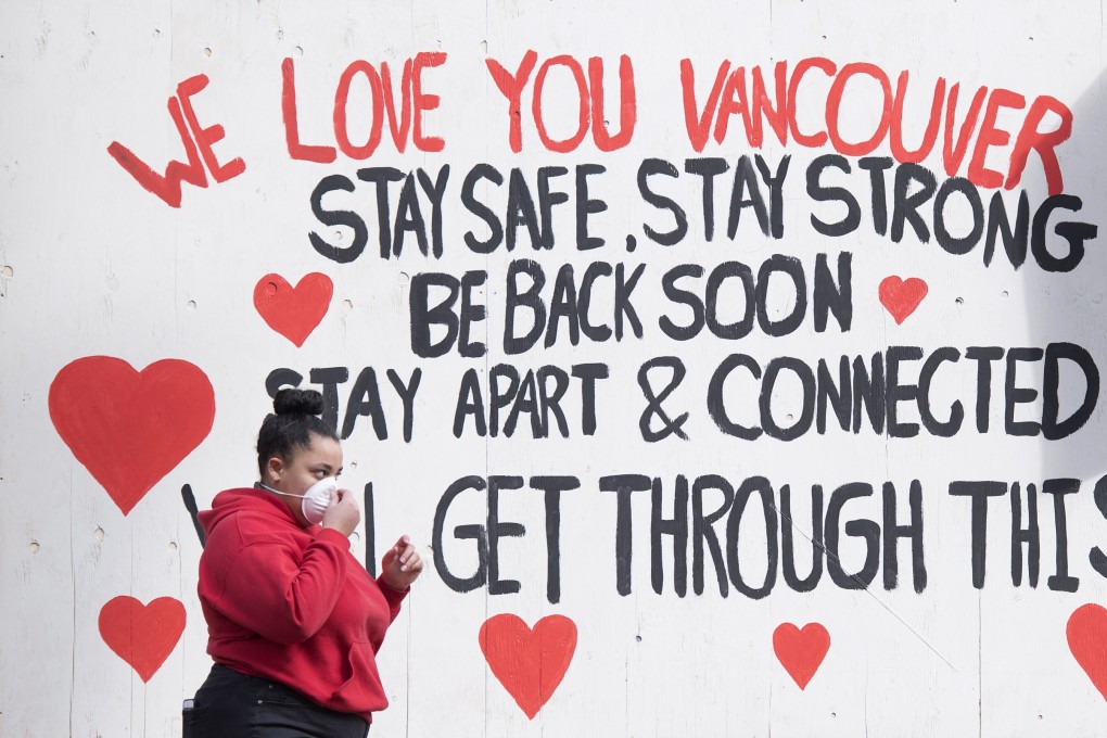 A woman wearing a protective face mask walks past a message painted on a boarded-up business in downtown Vancouver on Wednesday. Photo: AP