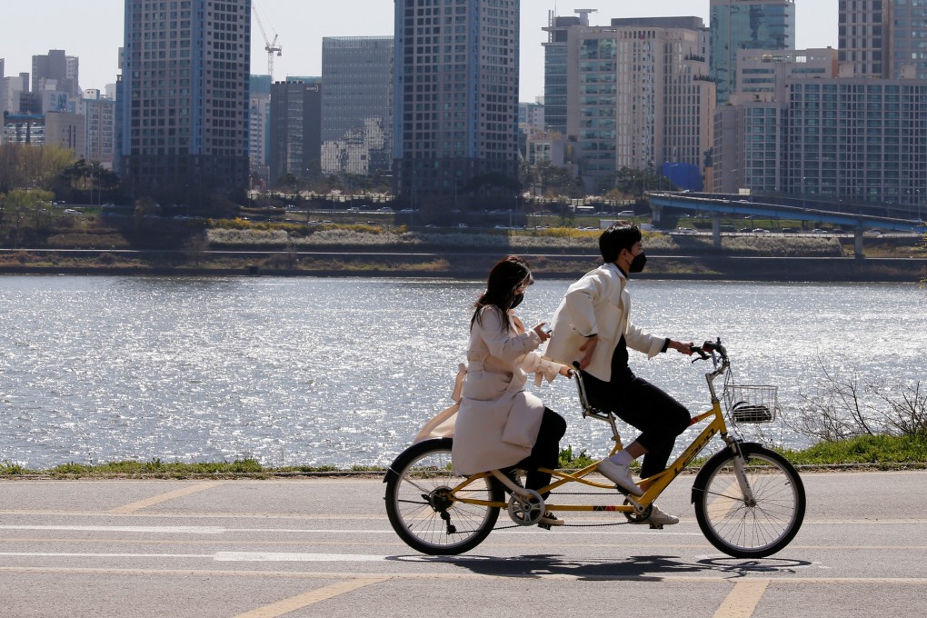 A couple wearing masks ride on a bicycle at a Han River Park in Seoul on April 4, 2020. Photo: Reuters