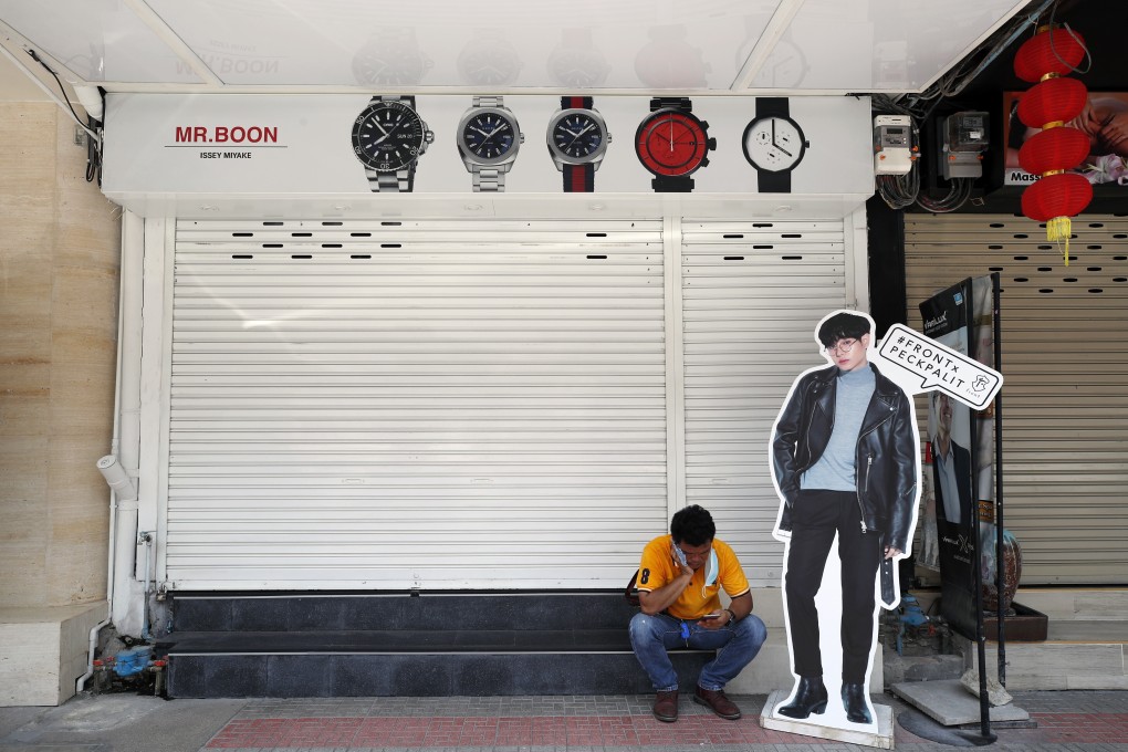 A Thai man uses his mobile phone in a deserted street in Bangkok after shopping centres were closed to prevent the spread of Covid-19. Photo: EPA