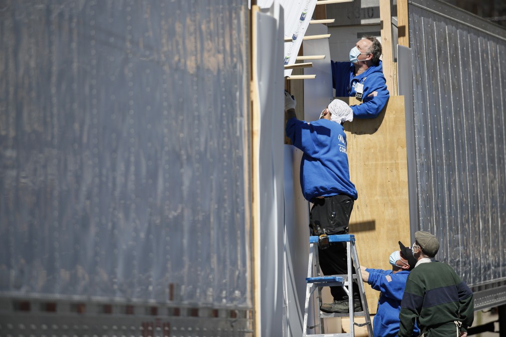 Workers build a barrier to obstruct the street-level view of a loading platform leading into refrigerated trailers serving as a makeshift morgue in New York on Monday. The trailers are also running out of room. Photo: AP