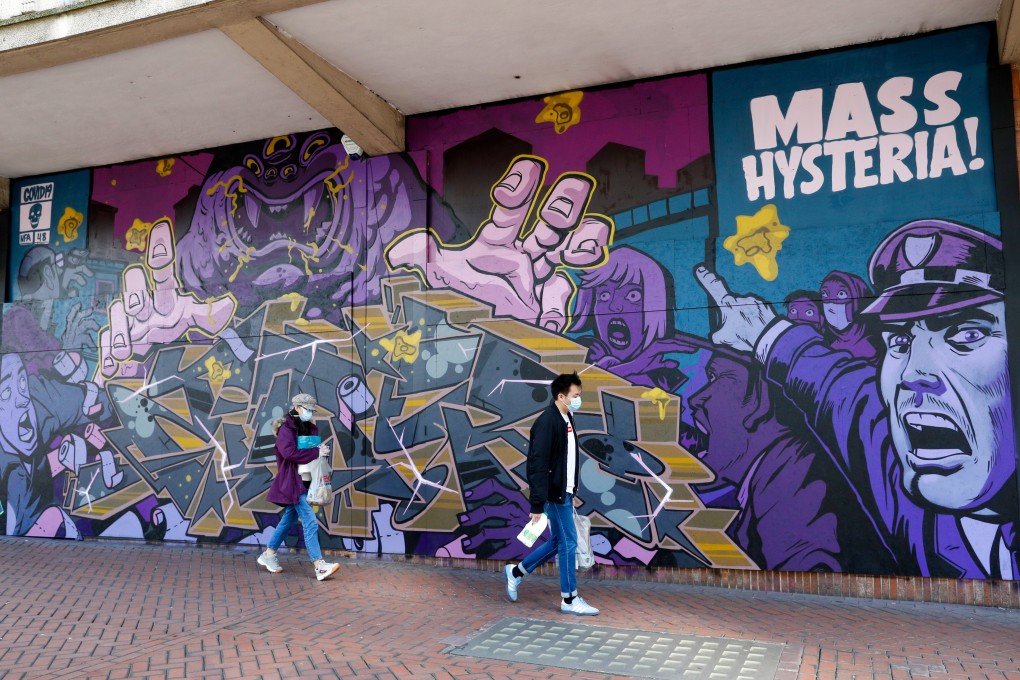 Pedestrians wearing protective masks walk past a street art mural depicting "Mass Hysteria" related to the Covid-19 pandemic in Birmingham, UK on April 6, 2020. Photo: Bloomberg