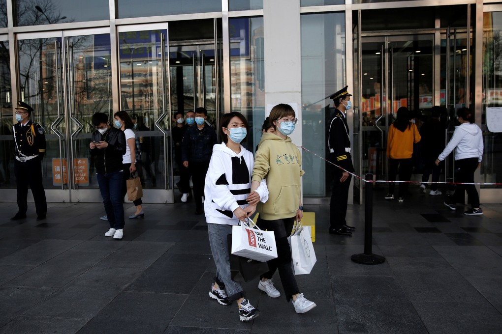 Shoppers with face masks walking out of a mall in Beijing as the pandemic shrinks the nation’s much-vaunted army of consumers. Photo: Reuters