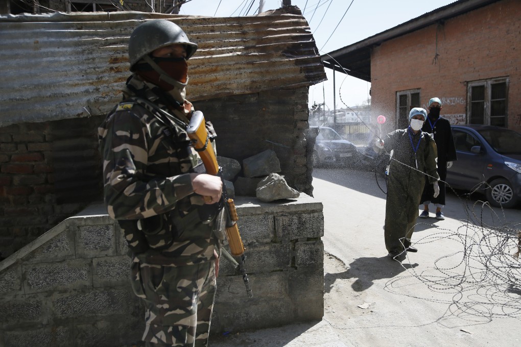 An Indian soldier stands guard as a Kashmiri volunteer sprays disinfectant as a precautionary measure against the coronavirus in Srinagar. Photo: AP