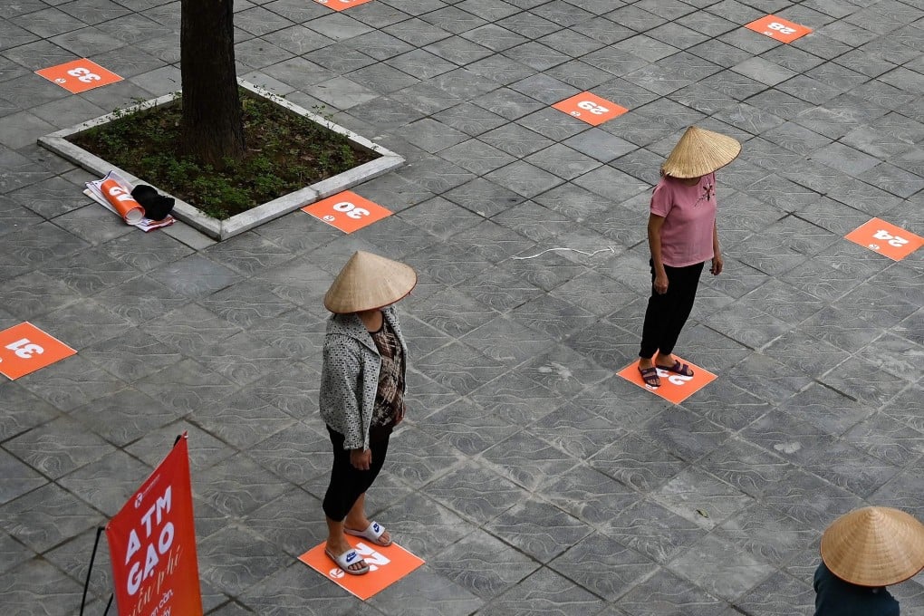 Residents wearing face masks practice social distancing as they wait in a queue for free rice in Hanoi. Photo: AFP