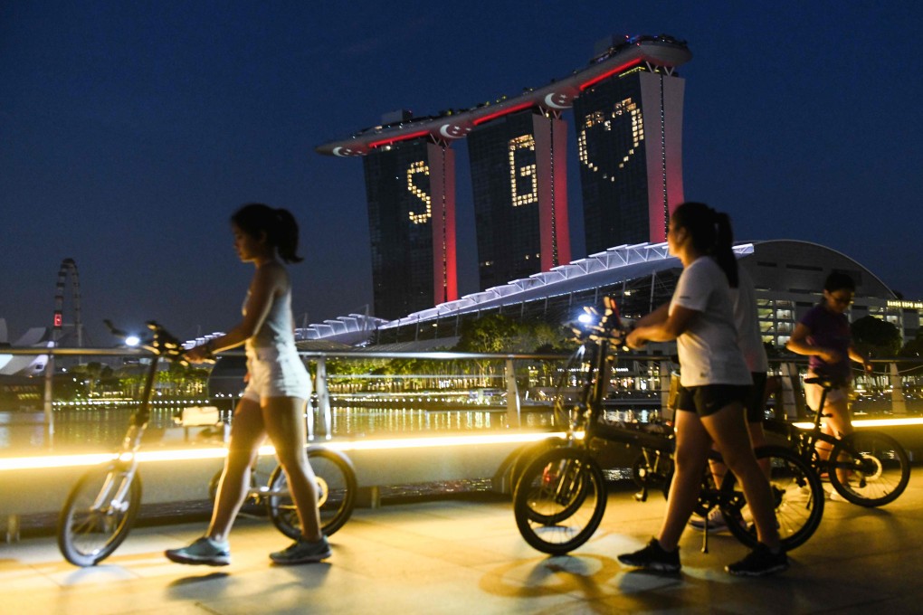 People walk by with their bicycles as Marina Bay Sands lights up with a message of hope on April 10, 2020. Photo: AFP