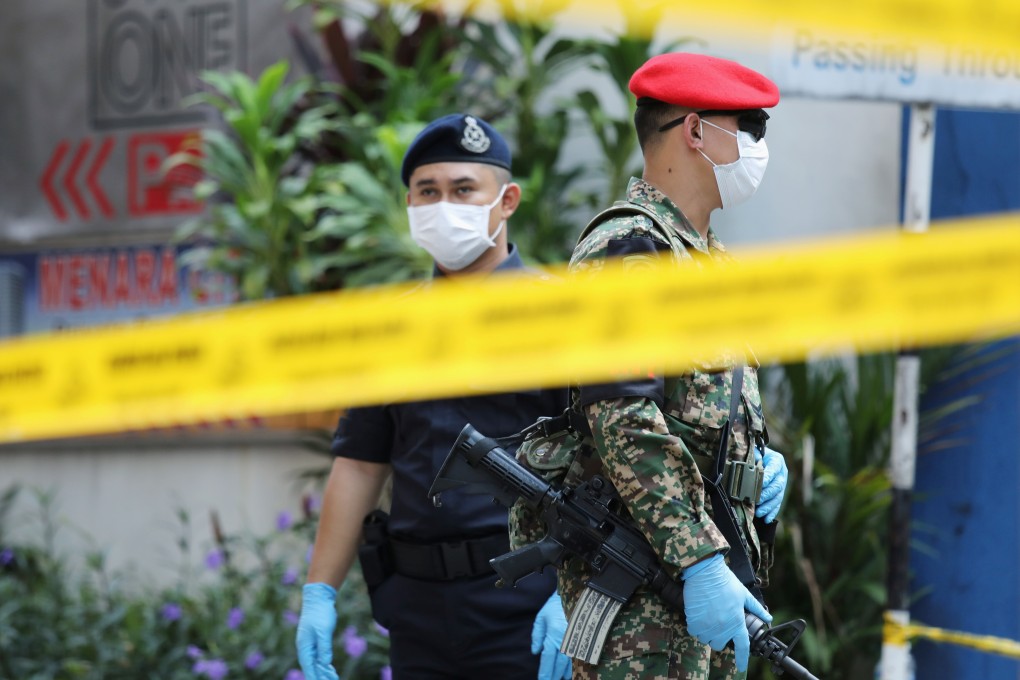 A Malaysian police officer and soldier are seen behind a yellow tape. Malaysian police have arrested 14 Chinese nationals in a cryptocurrency scam. Photo: Reuters