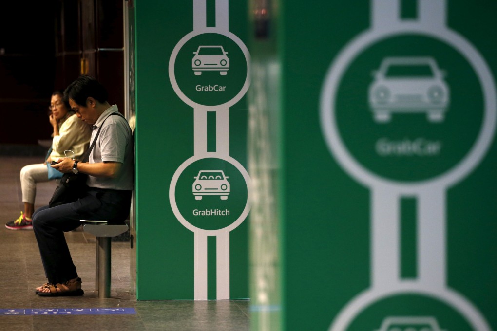 Commuters wait next to Grab’s transport booking service app advertisements at a railway station in Singapore in February of 2016. Photo: Reuters